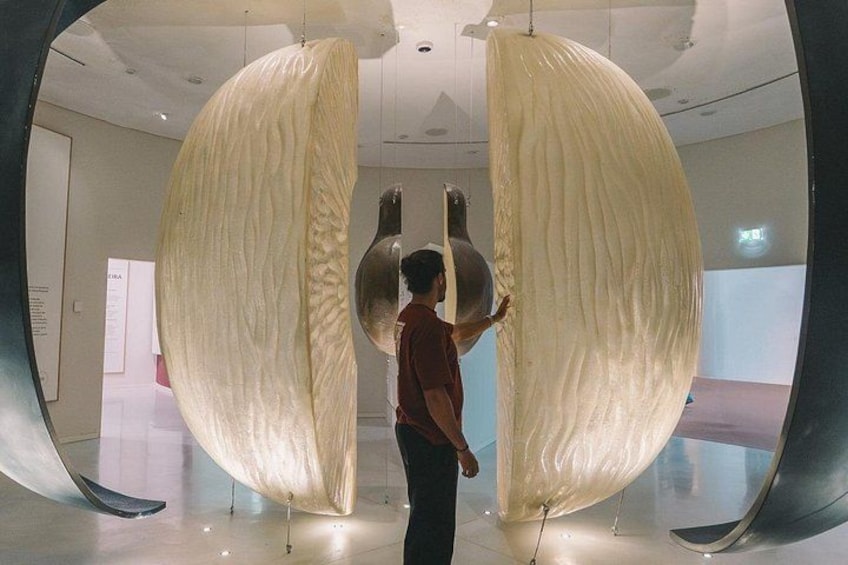 A person standing in a modern art gallery, observing a large, textured sculpture. 2