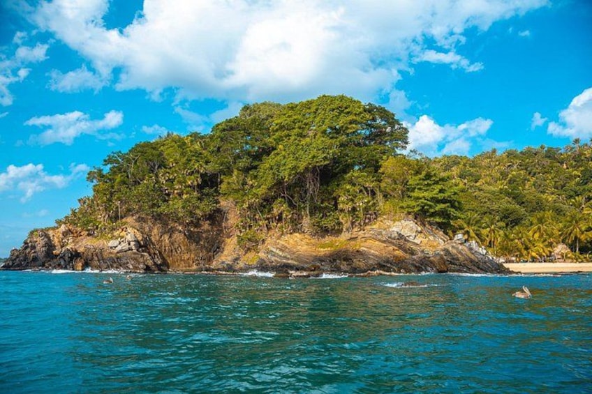 A tropical island with clear blue waters, a rocky coastline, and dense green vegetation. 5