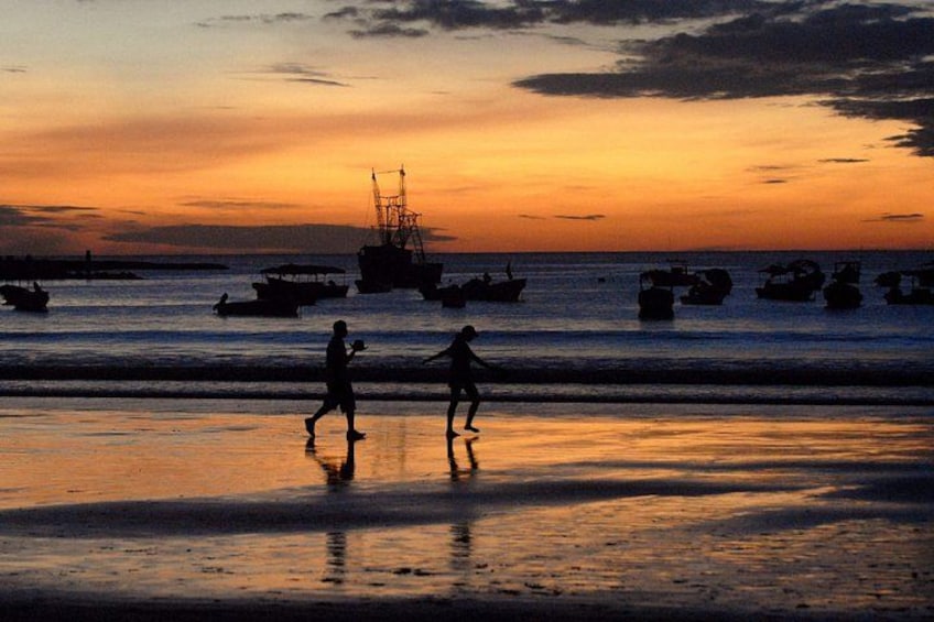 A sunset over a beach with silhouettes of people and boats. 5