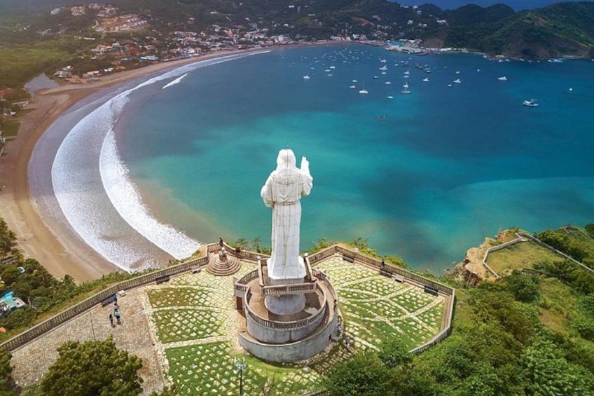 A coastal statue, a beach, and a harbor with boats. 1