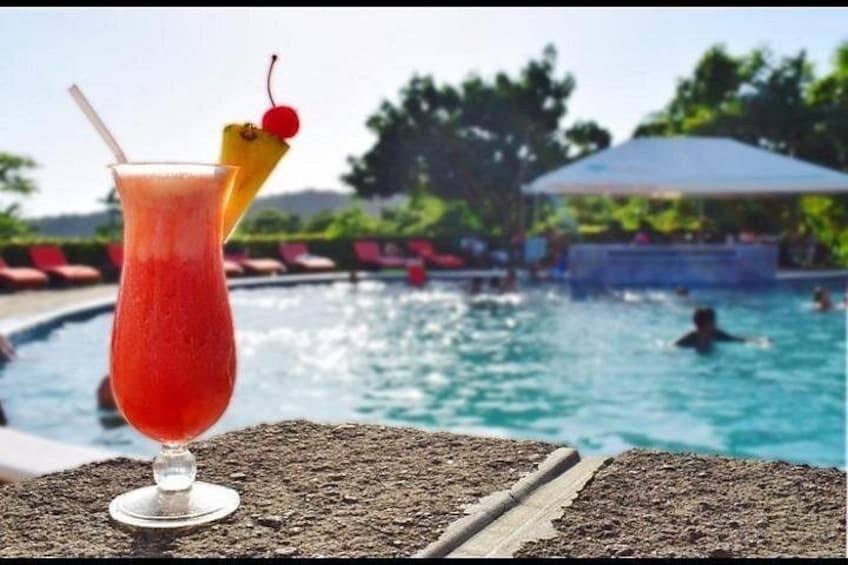 A poolside with a drink in a glass, a pool, and people swimming. 3