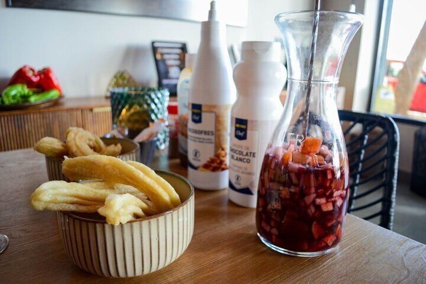 Eine Küchenarbeitsplatte mit einer Schüssel Churros, einer Flasche Schokoladensauce und einem Krug mit roter Flüssigkeit. 2