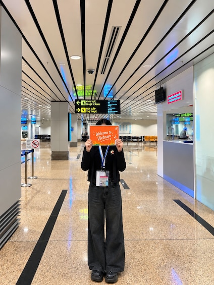 A person holding a sign that says 'Welcome to Vietnam' in an airport terminal with directional signs and a digital display. 4