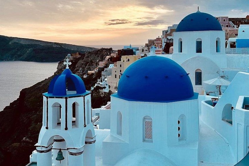 A coastal town with white buildings and blue domes, overlooking the sea. 3