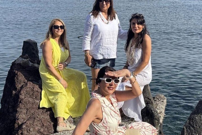 A group of people sitting and standing on rocks by a body of water. 4