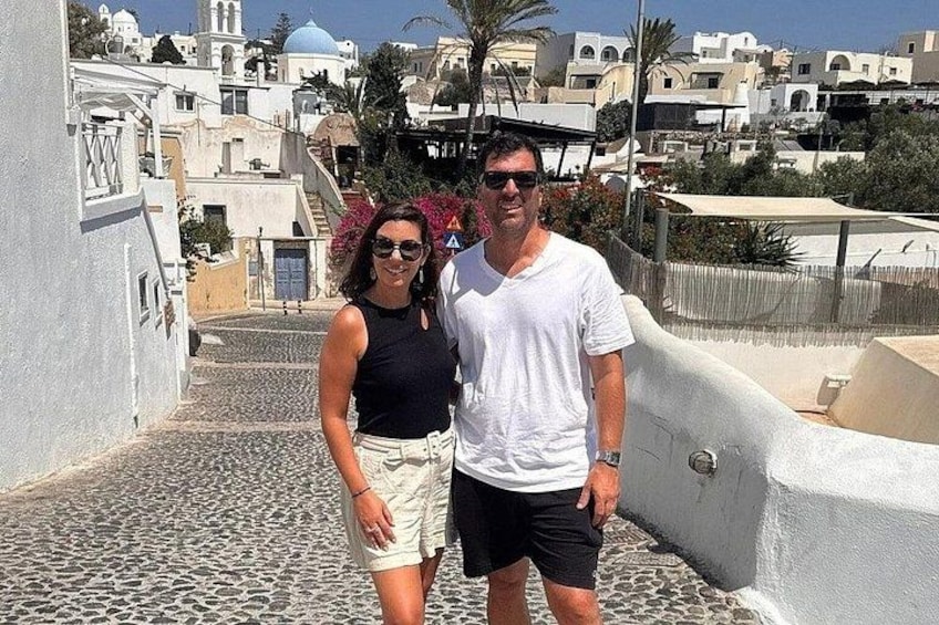 A couple standing on a cobblestone street with white buildings and blue domes in the background. 2