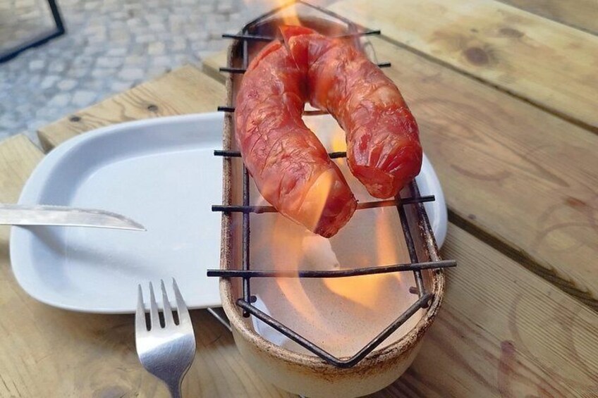 A grilled sausage on a metal rack over a white plate, with a fork and knife beside it. 5