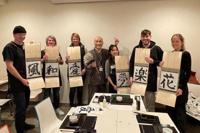 Un groupe de personnes tenant des sacs en papier ornés de caractères japonais, se tenant dans une pièce où une table expose divers objets. 2