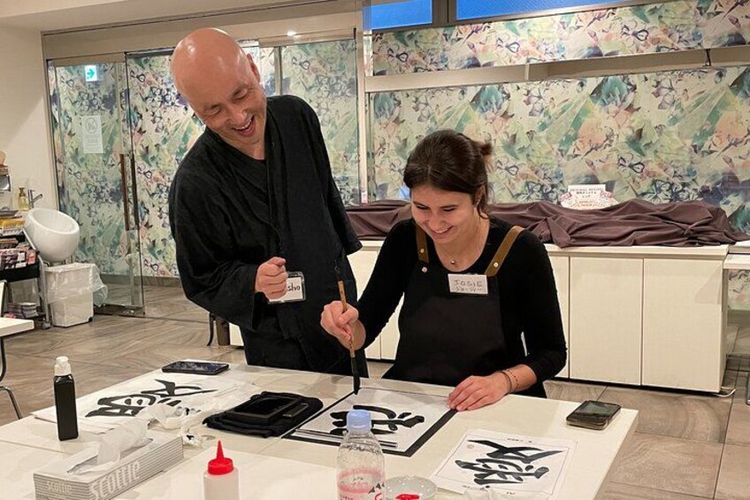 Two people painting calligraphy on paper at a table with brushes, ink, and paper. 1