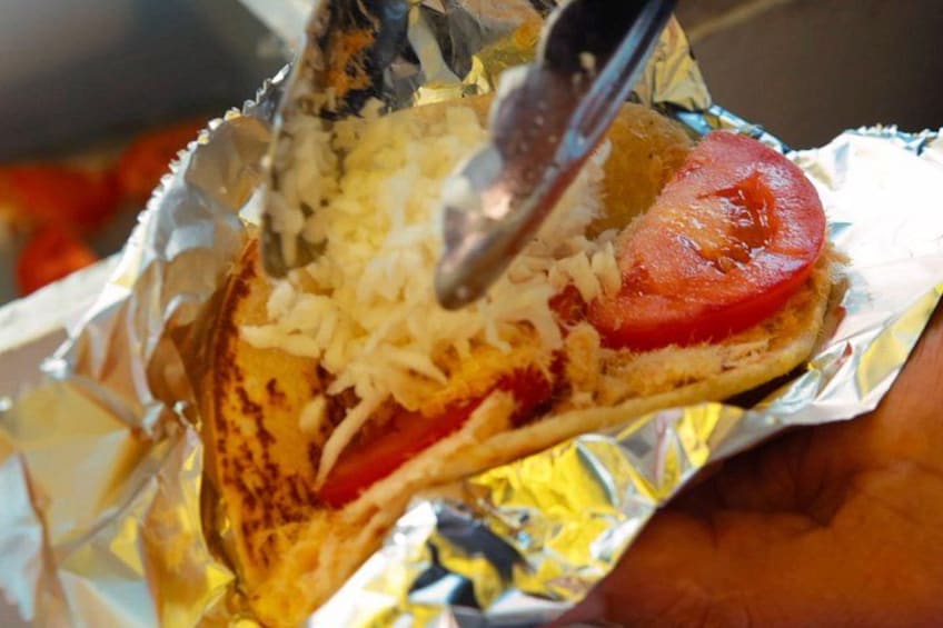 Un sándwich siendo preparado con queso y tomate envuelto en papel de aluminio. 3