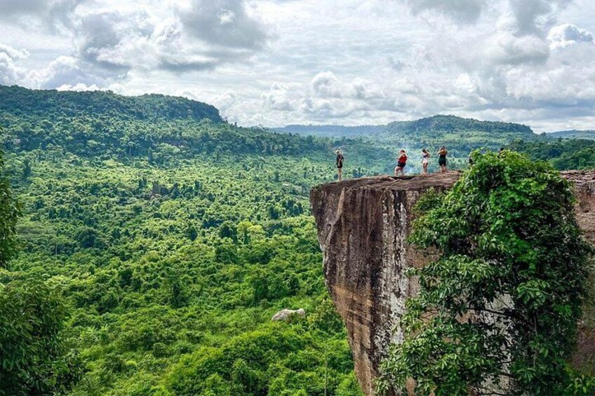 A cliff overlooking a dense forest with people standing on top. 2