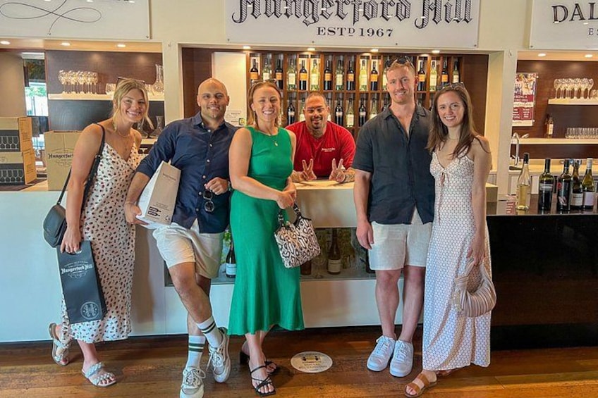 A group of people standing in front of a bar with shelves of bottles. 4