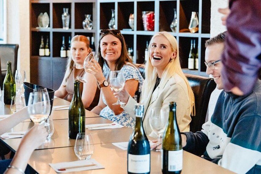 A group of people sitting at a table with wine bottles and glasses. 5