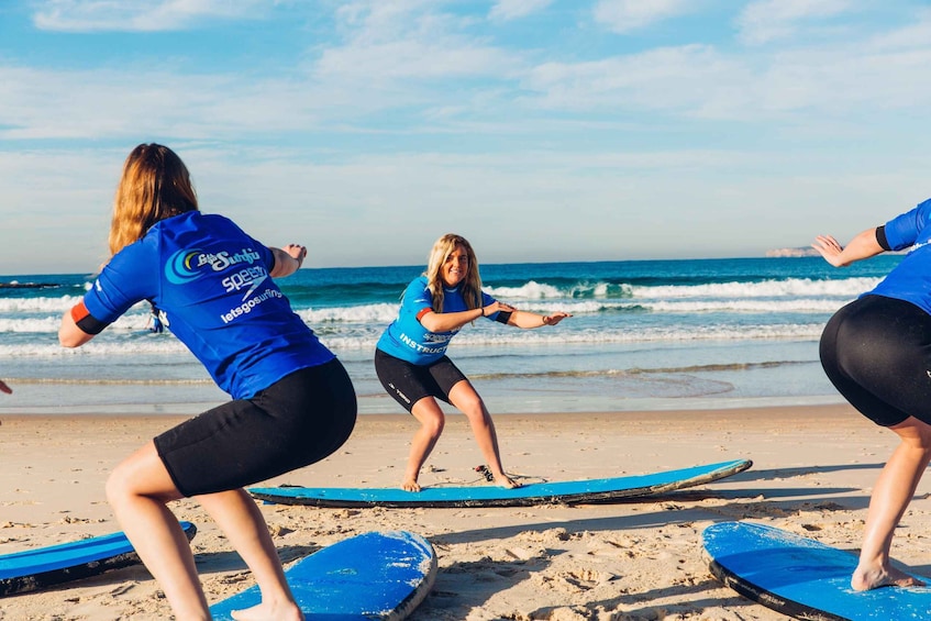 Three people practicing surfing on a beach with ocean waves in the background. 2