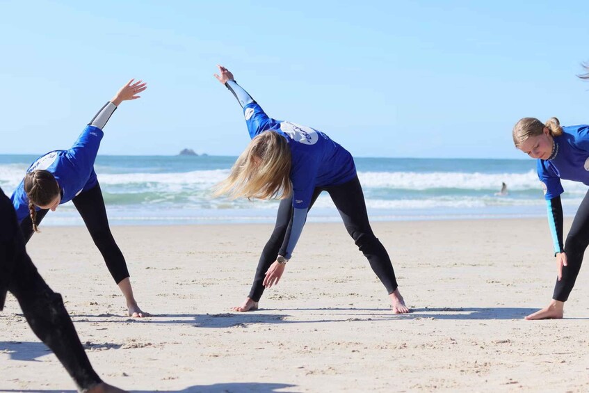 Three people in blue wetsuits practicing surfing on a beach with waves. 5