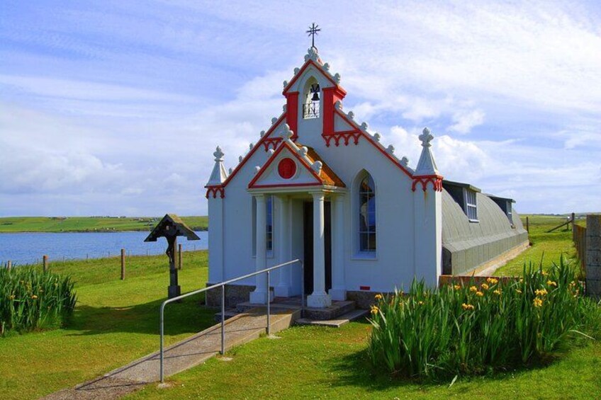 A small white church with a red roof and a bell tower, surrounded by grass and flowers. 4