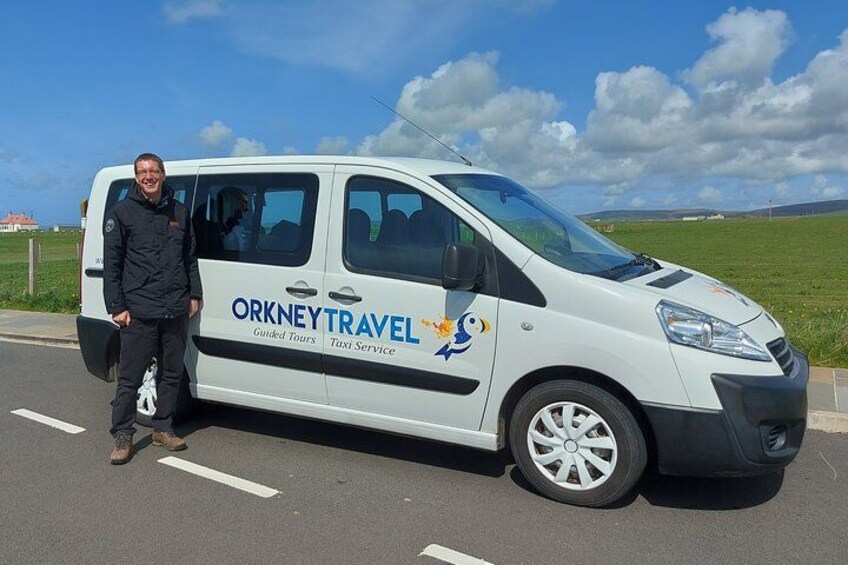 A white van with ORKNEYTRAVEL branding parked on a road. 3