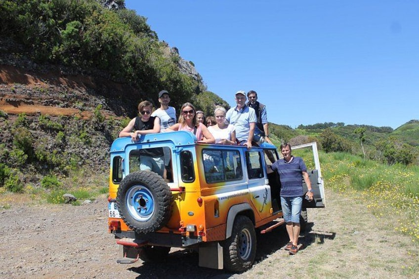 Un groupe de personnes se trouve à bord d’un véhicule tout-terrain jaune et bleu, dans un environnement naturel caractérisé par la présence de verdure et de collines. 4