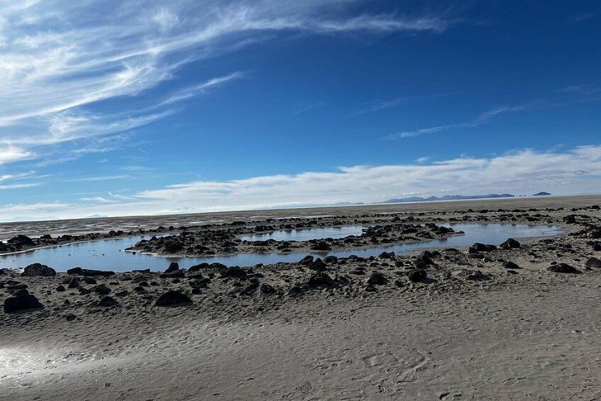 A coastal landscape with a sandy beach, scattered rocks, and small water pools. 3