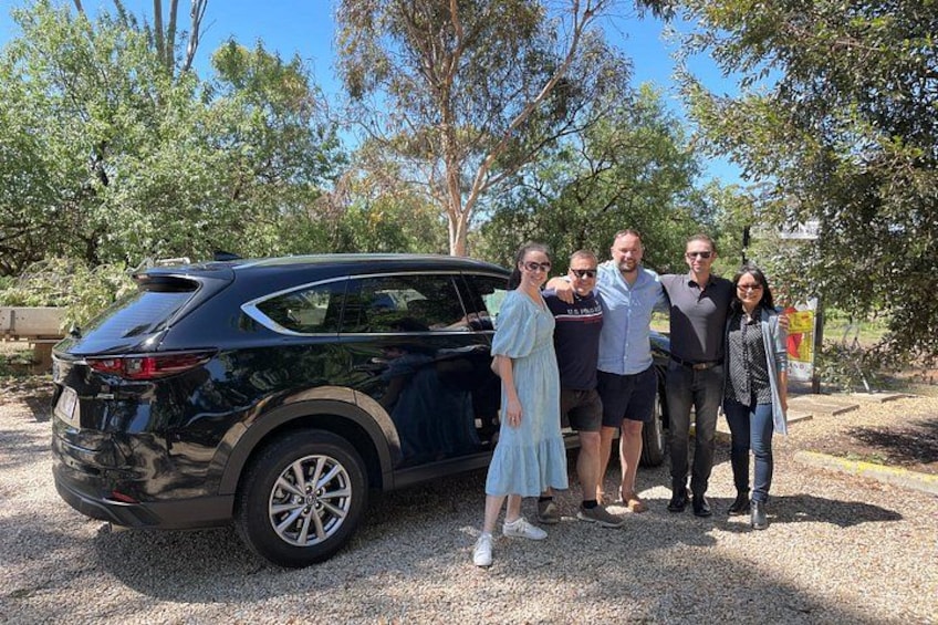 A group of people standing beside a black SUV on a gravel surface with trees in the background. 4