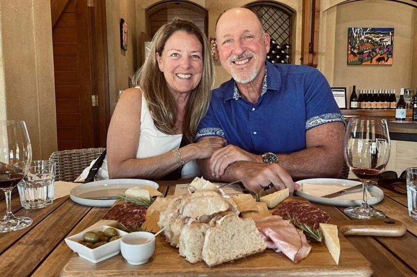 A couple seated at a wooden table with a charcuterie board, wine glasses, and a bottle of wine. 5