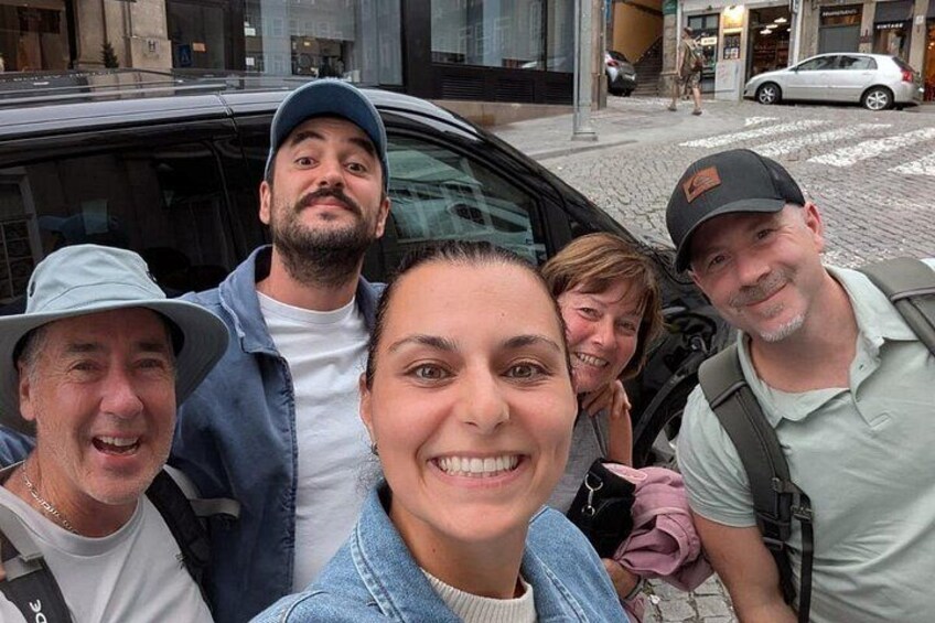 A group of people standing in front of a car on a city street. 2