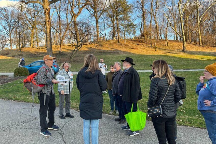 Eine Gruppe von Personen steht auf einem gepflasterten Weg in einem Park, im Hintergrund sind Bäume zu sehen. 2