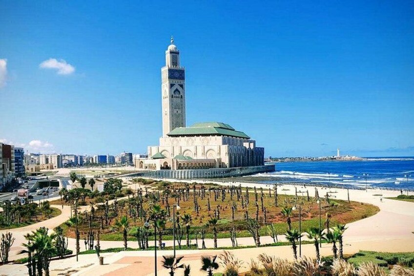 A coastal cityscape with a prominent mosque featuring a tall minaret, palm trees, and a beach. 3