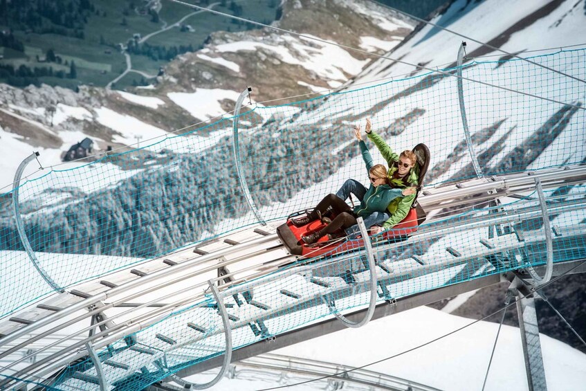 A person on a red sled sliding down a snowy slope with a safety net. 3