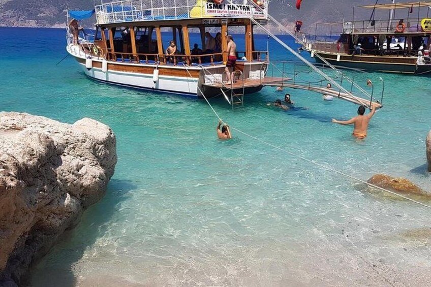 A boat with people swimming in the water, a rocky shore, and another boat in the background. 5