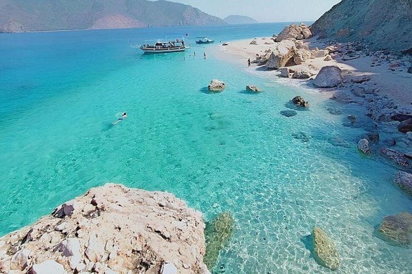 A clear turquoise sea, rocky shoreline, and a boat in the distance. 1