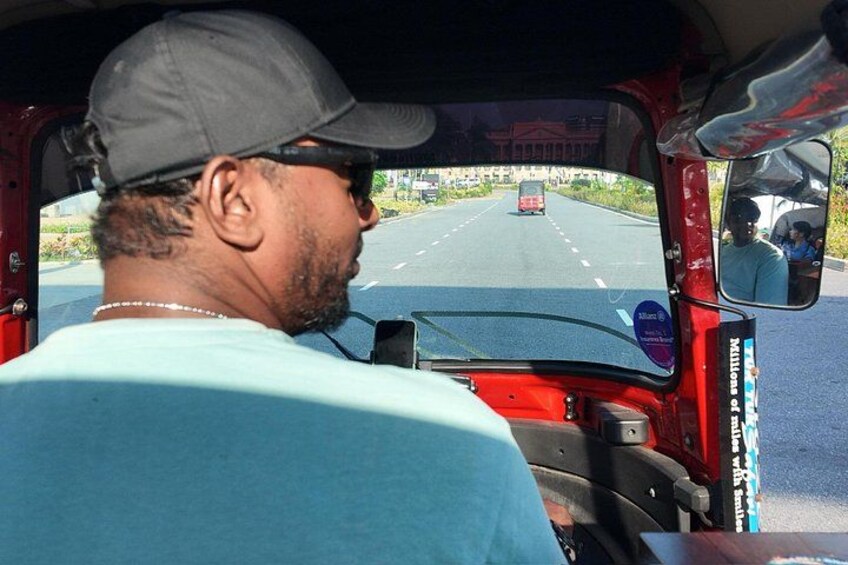 A man driving a red auto-rickshaw on a road with a clear sky. 2
