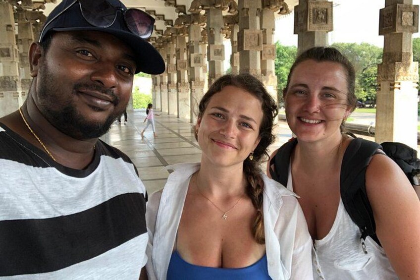 Three people standing under a structure with columns and a person walking in the background. 4