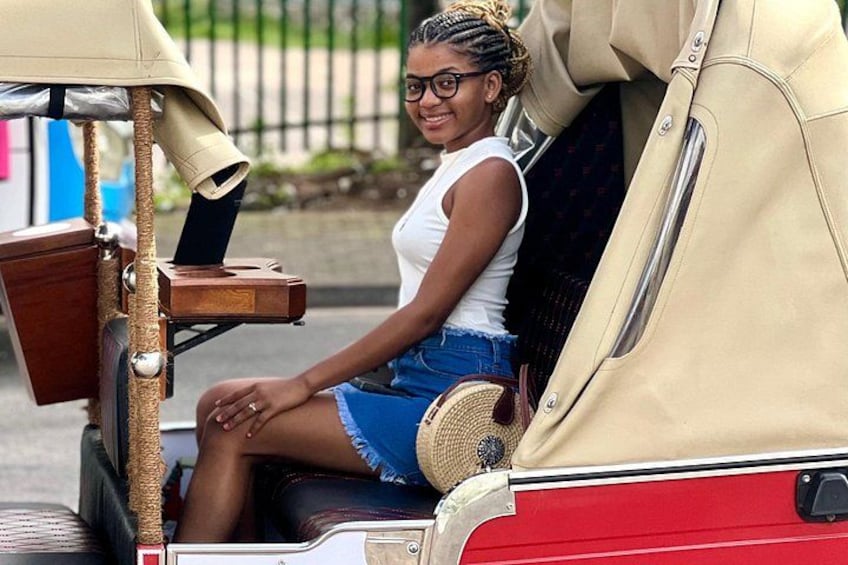 A woman in a white tank top and denim shorts sitting in a vintage red car with a beige roof. 5