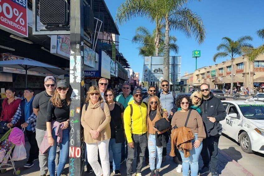A group of people standing on a street with palm trees and shops in the background. 3