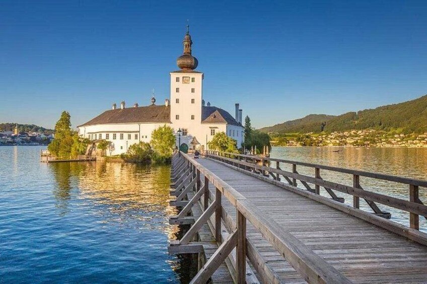 A wooden bridge leading to a white building with a tower by a calm lake. 2