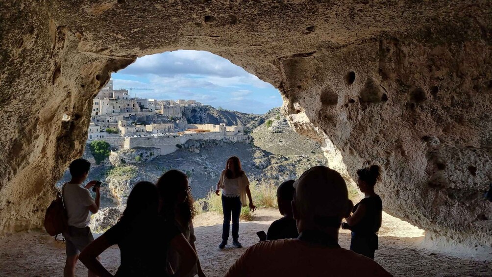 A group of people inside a cave observing a cityscape through a natural archway. 2