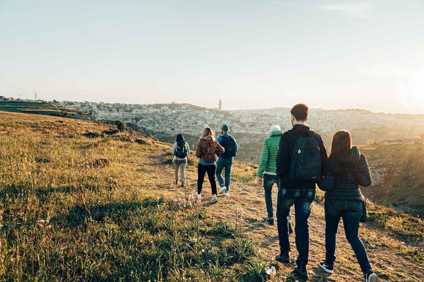 A group of people hiking on a grassy hill with a cityscape in the background. 1