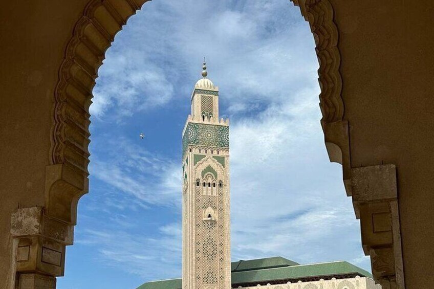 A tall tower with intricate patterns and a green dome, viewed through an archway. 4