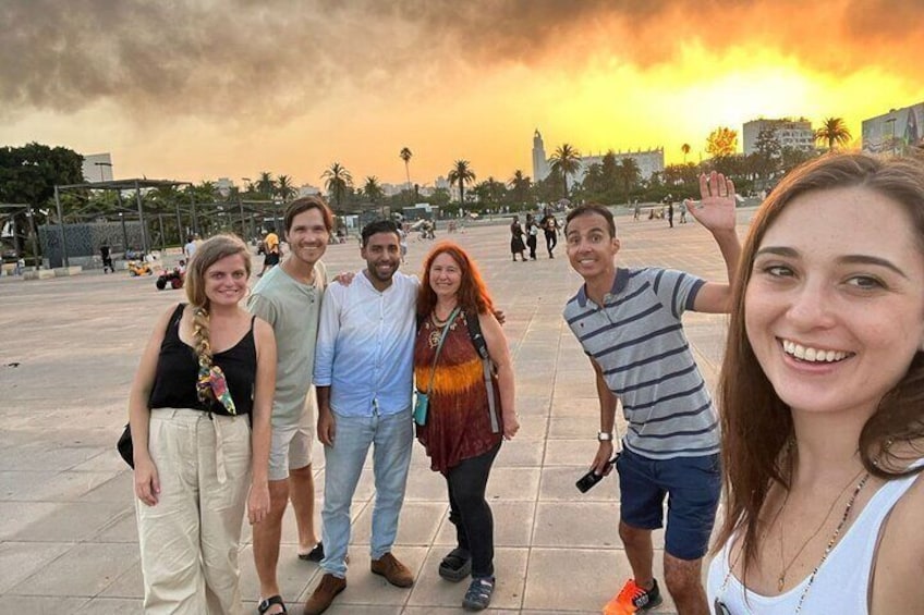 A group of people standing in a public square with a sunset in the background. 1