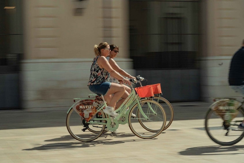 Deux personnes font du vélo sur une rue de la ville, sur un vélo ancien muni d’un panier rouge. 5