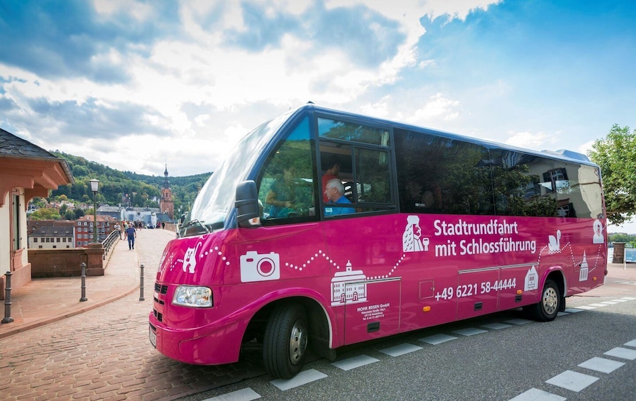 Un autobus touristique rose est garé sur une rue pavée, sous un ciel dégagé. 2