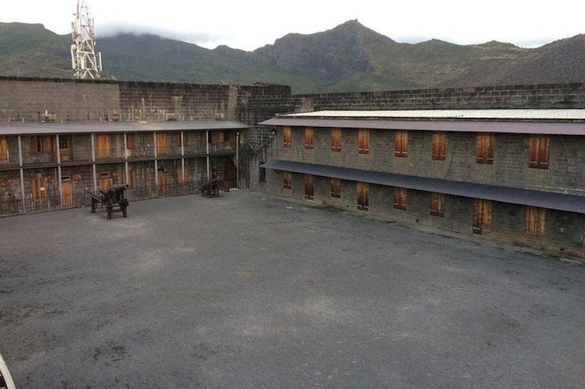 Un amplio patio descubierto con un edificio de múltiples ventanas y fachada de ladrillo, rodeado de montañas. 4