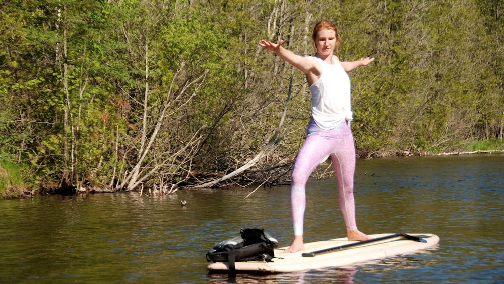 A person standing on a paddleboard in a river surrounded by trees. 5