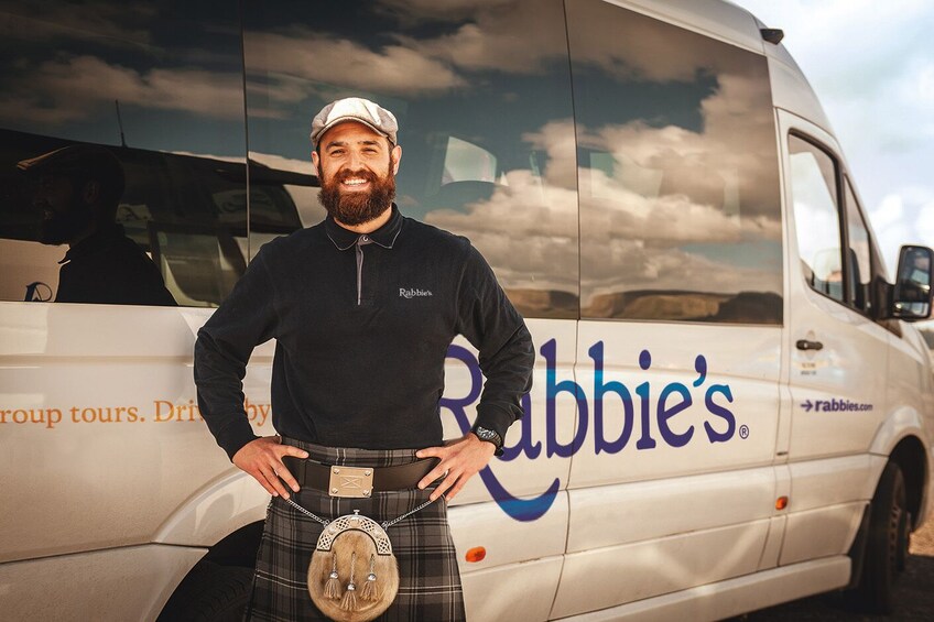 Un homme vêtu d’une chemise noire et d’un kilt se tient devant un fourgon blanc sur lequel on peut lire le mot « Rabbie’s ». 5