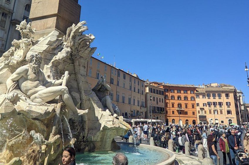 A historic fountain with sculptures, surrounded by a crowd of people and classic buildings. 2