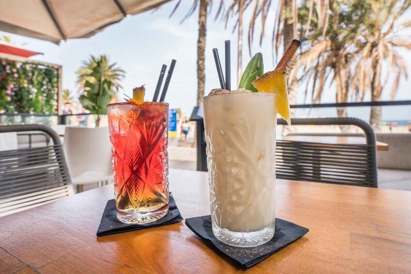 Two cocktails on a wooden table with a beach and palm trees in the background. 4