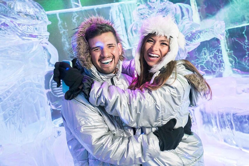 Two people embracing in a snowy setting with ice sculptures. 1