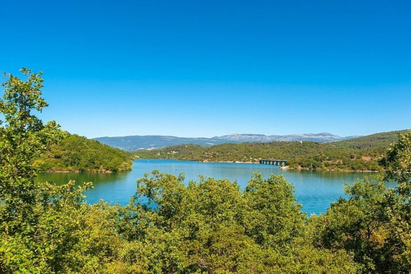 Ein See, umgeben von Hügeln, einer Brücke und dichtem Grün. 1