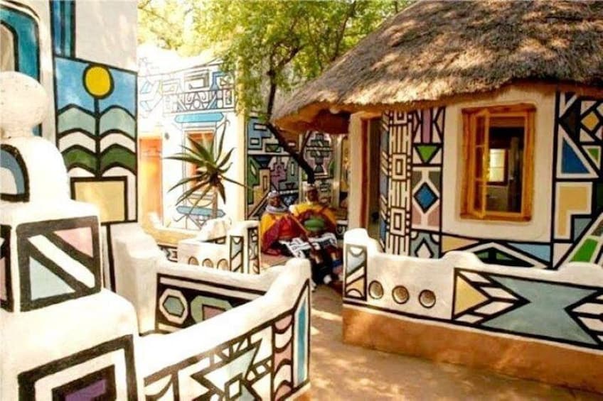 A traditional house with colorful geometric patterns, a thatched roof, and a person sitting outside. 2
